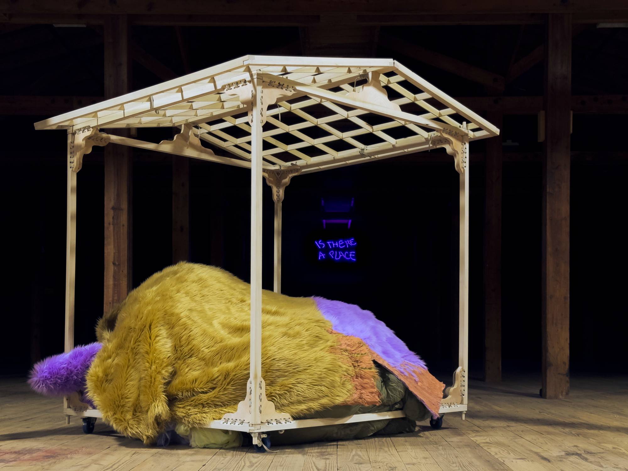 Yellow furry object under off-white pavilion dramatically lit with colorful background.